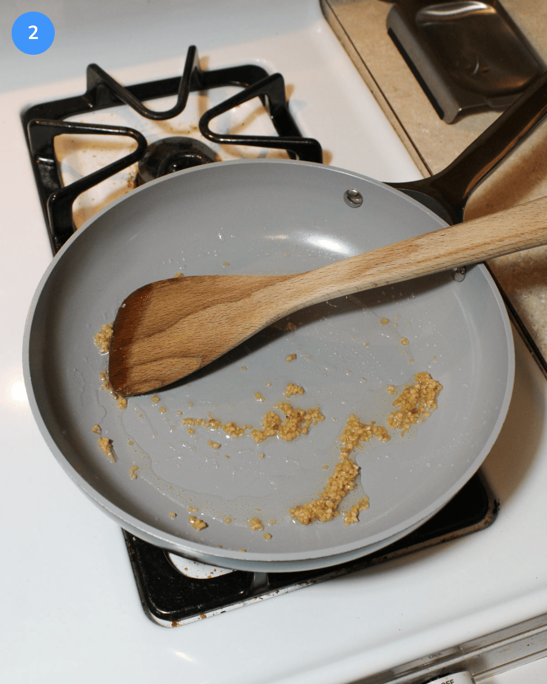 A ceramic frying pan with olive oil and minced garlic cooking on the stove.