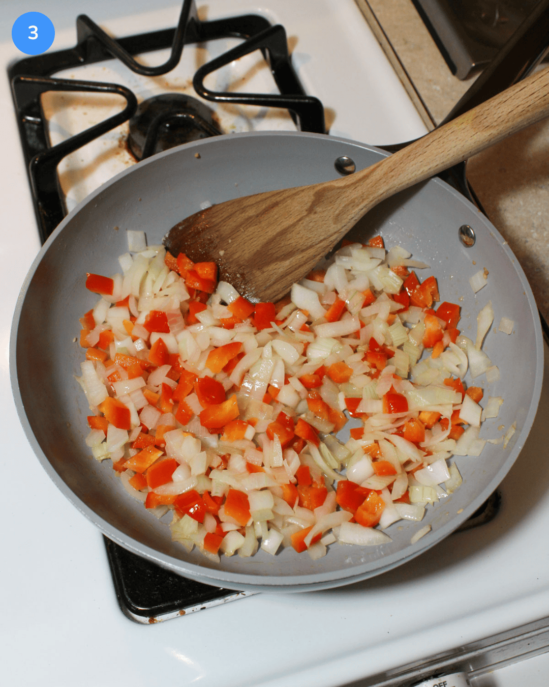 A ceramic frying pan filled with diced onion and red bell pepper, sauteeing on the stove.