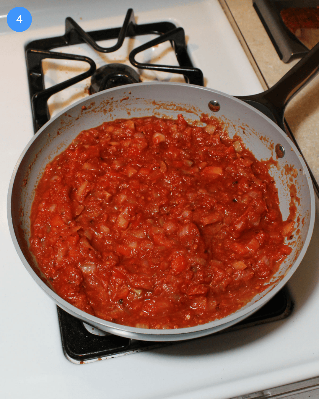 A ceramic frying pan with tomato, pepper, and onion sauce simmering in it on the stove.