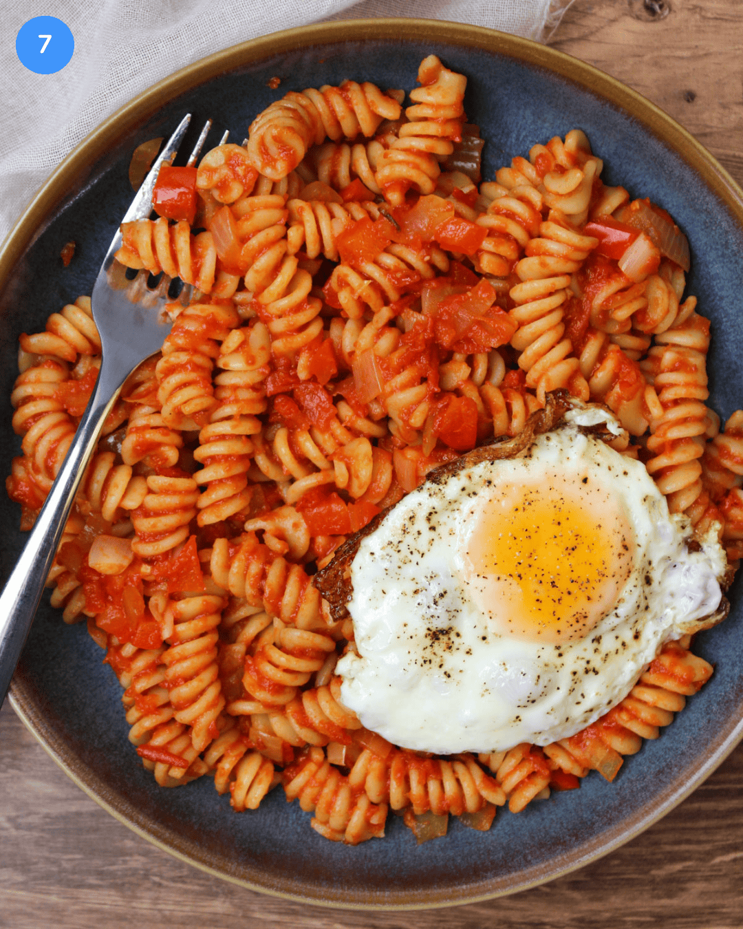 A blue stone bowl of shakshuka pasta served with an over medium egg.