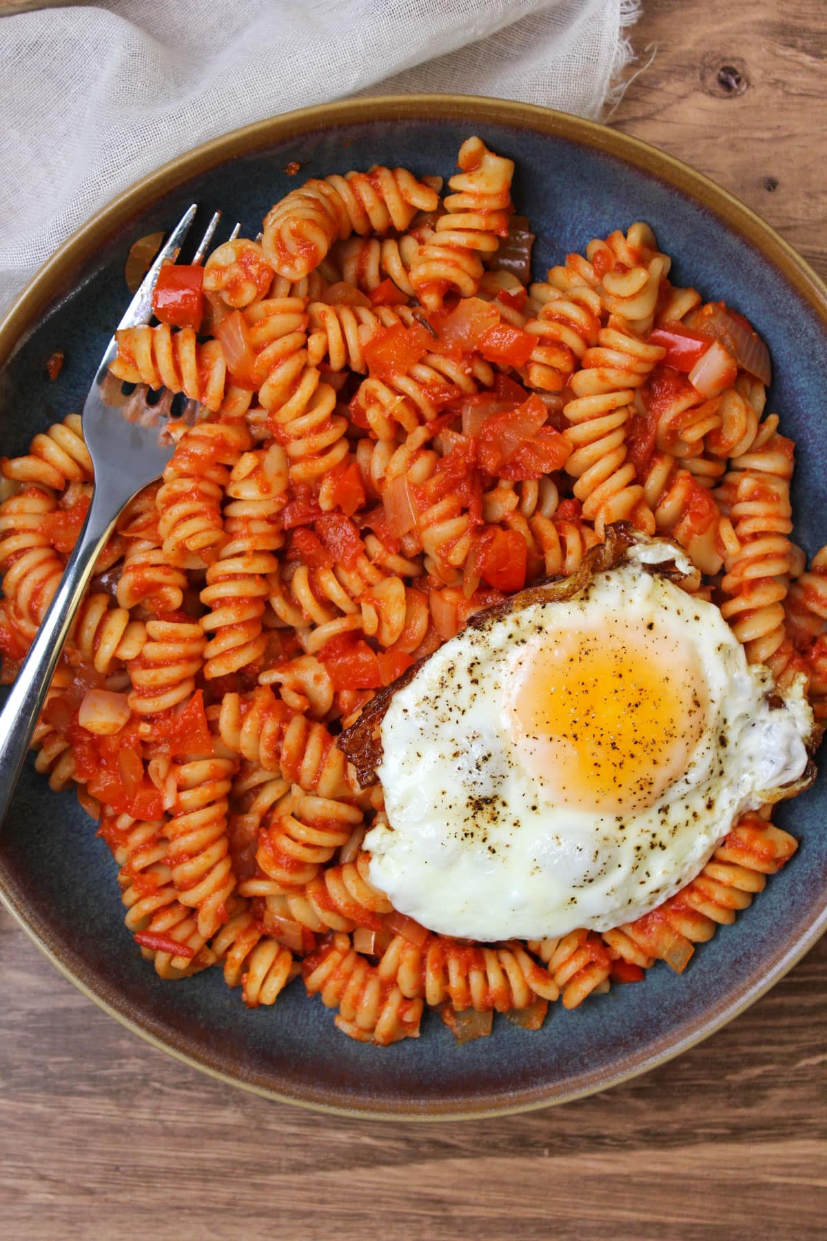 A blue stone bowl of shakshuka pasta served with a freshly fried egg.