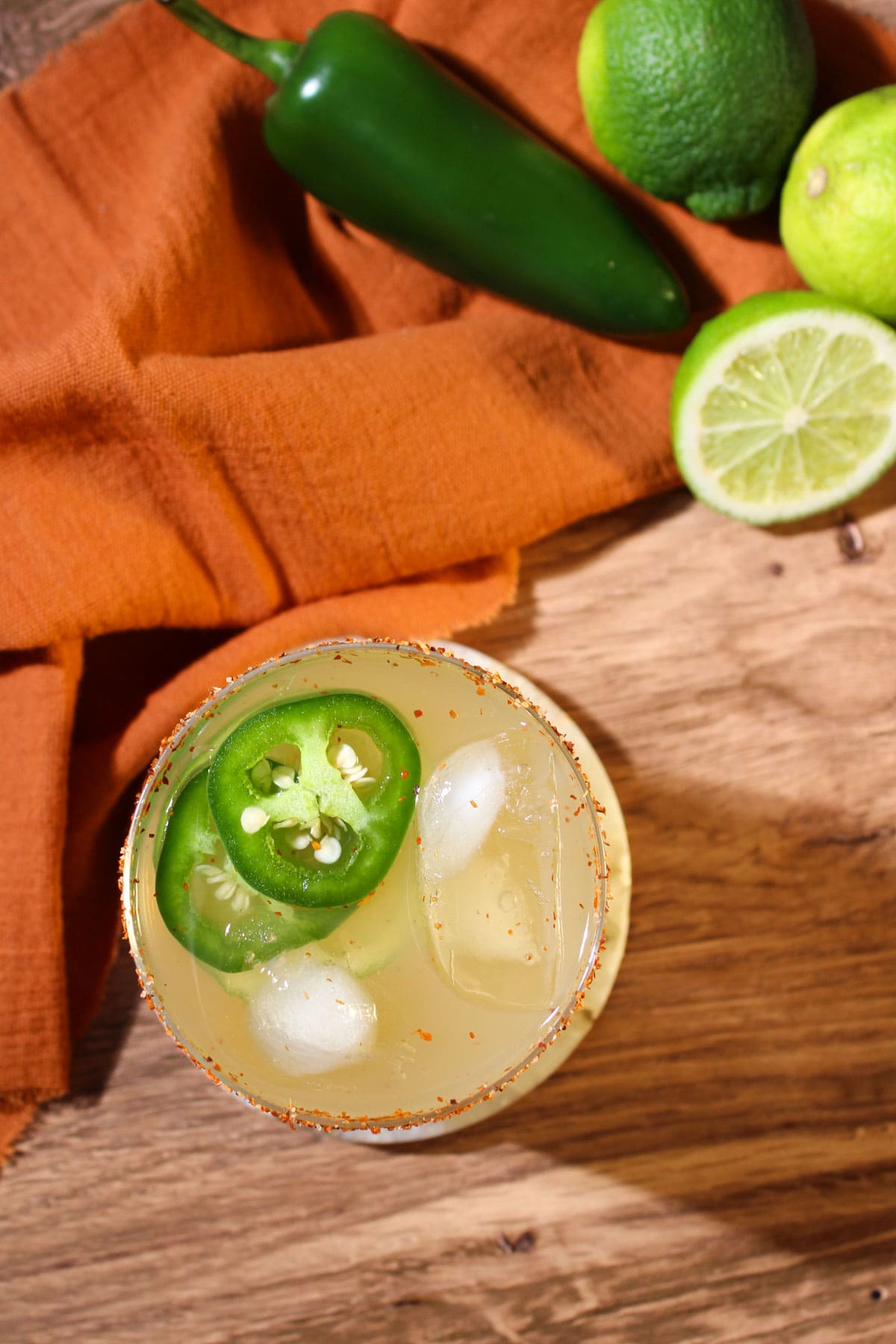 A mezcal margarita garnished with a Tajin rim and jalapeno wheels.