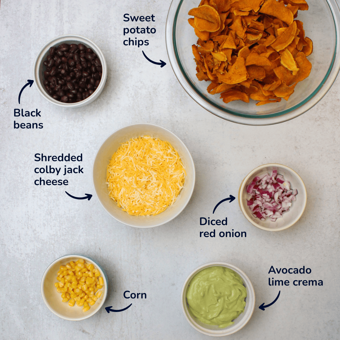 Ingredients for sweet potato nachos: sweet potato chips, black beans, corn, shredded mexican cheese, diced red onion, and avocado lime crema.