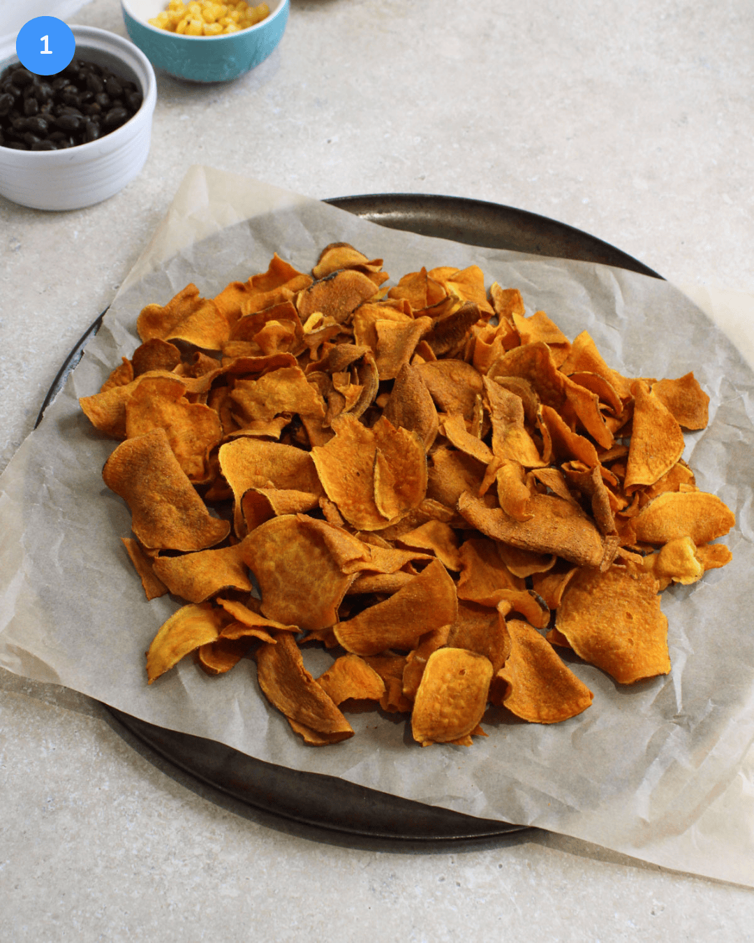 A round baking pan with parchment paper and a single layer of sweet potato chips on it.