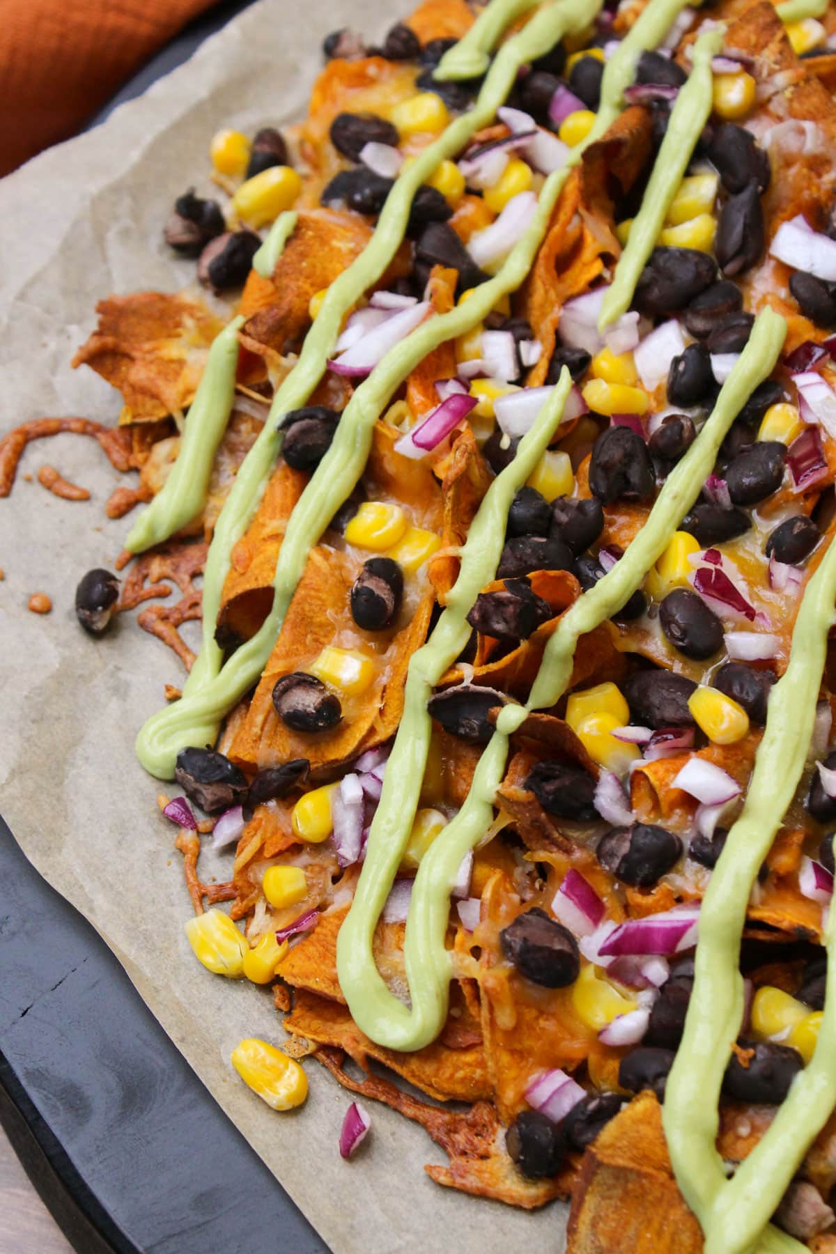 Freshly baked sweet potato nachos with gooey cheese, beans, corn, red onion, and creamy avocado lime crema drizzle.