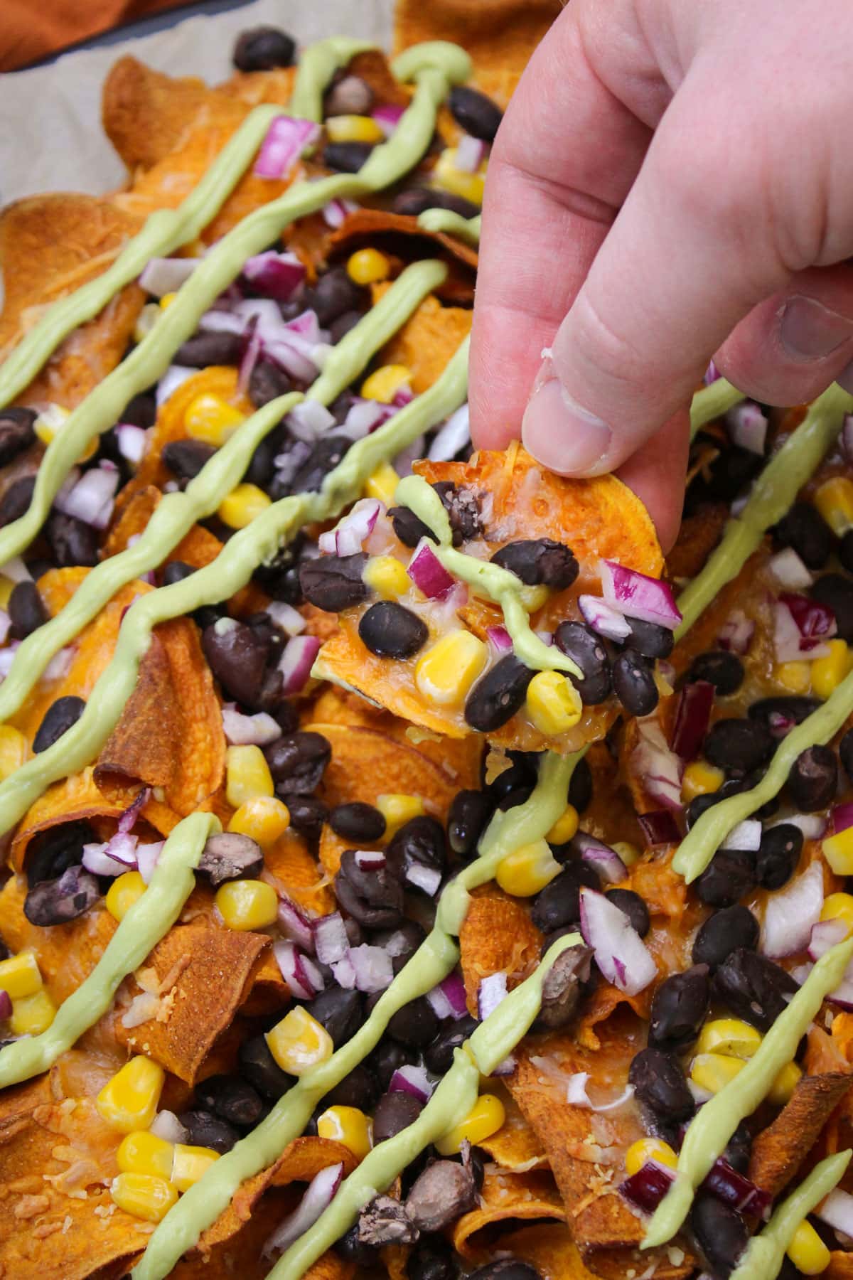 A sweet potato nacho chip topped with cheese, beans, corn, red onion, and avocado lime crema.