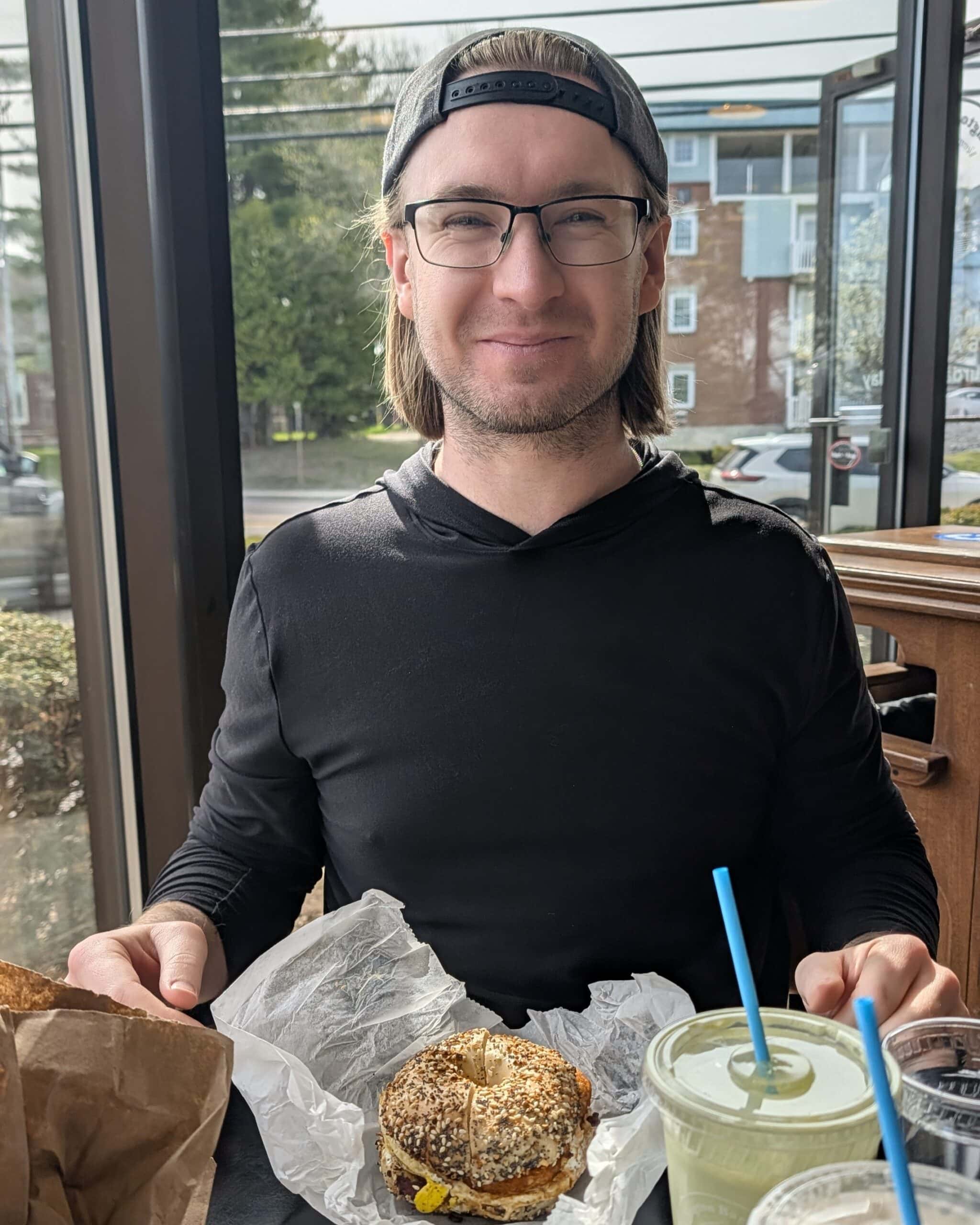 Alex at a bagel shop with a breakfast sandwich and iced matcha latte.