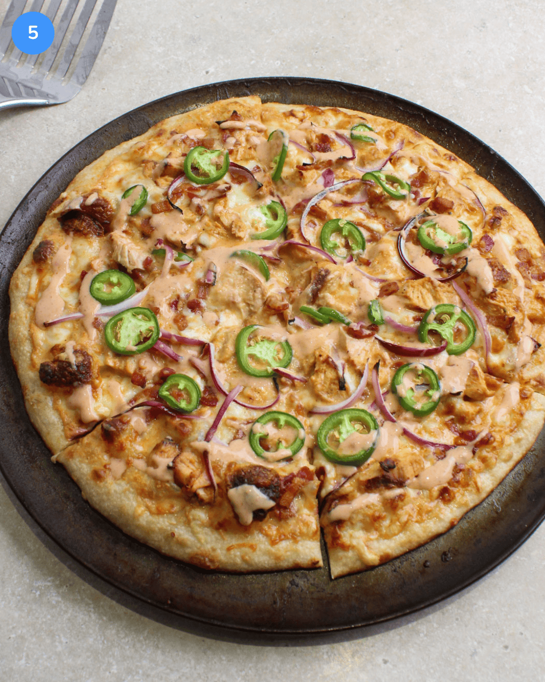 A freshly baked spicy chicken bacon ranch pizza on a round pan.
