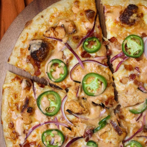 A freshly made chicken bacon ranchero pizza topped with jalapeno wheels and sliced red onion, served on a wooden pizza peel.