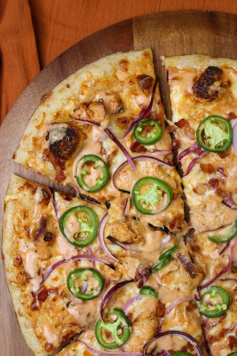 A freshly made chicken bacon ranchero pizza topped with jalapeno wheels and sliced red onion, served on a wooden pizza peel.