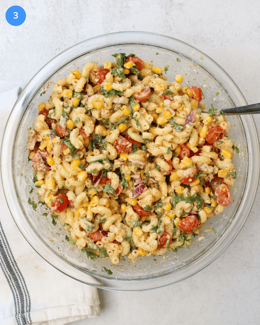 A large glass mixing bowl with freshly mixed elote pasta salad in it.