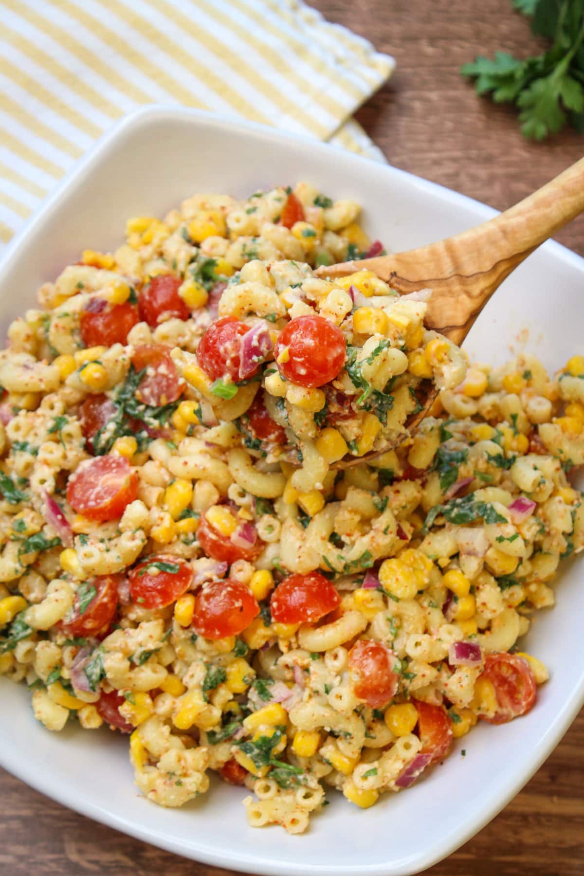 A wooden spoonful of elote pasta salad with tomatoes, onion, corn, and fresh cilantro.