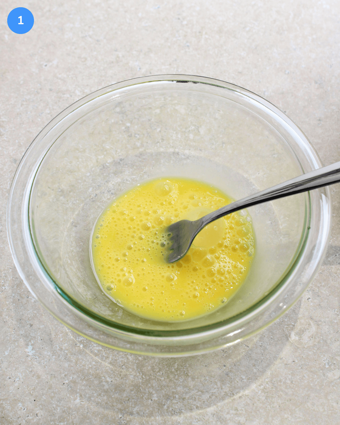 A small glass bowl with freshly beaten egg in it.
