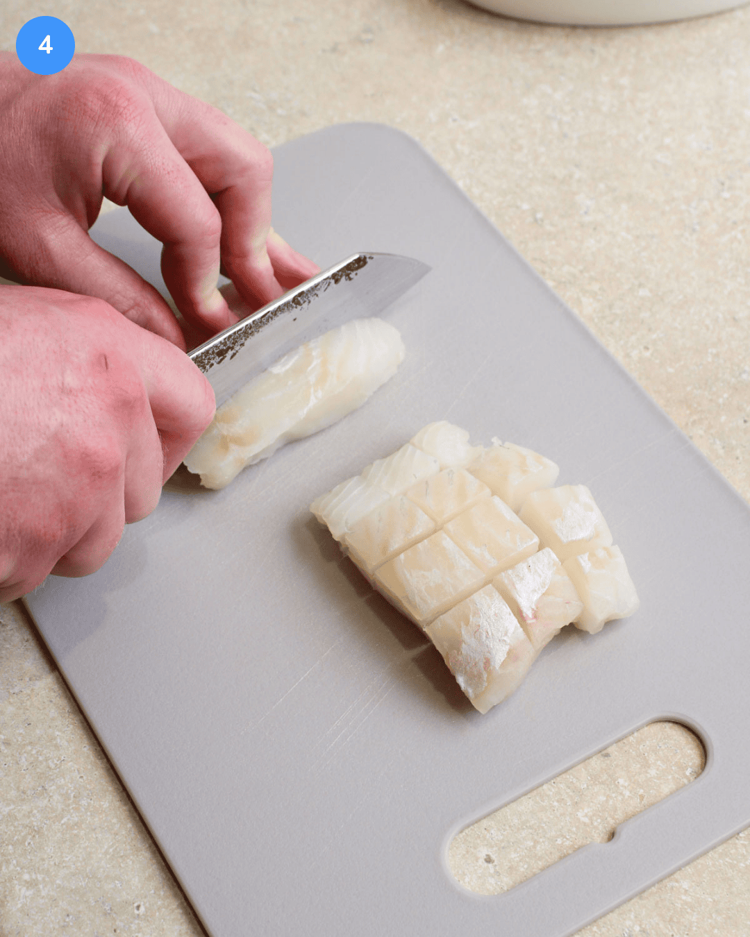 Cod fillets being sliced into small cubes on a gray cutting board.