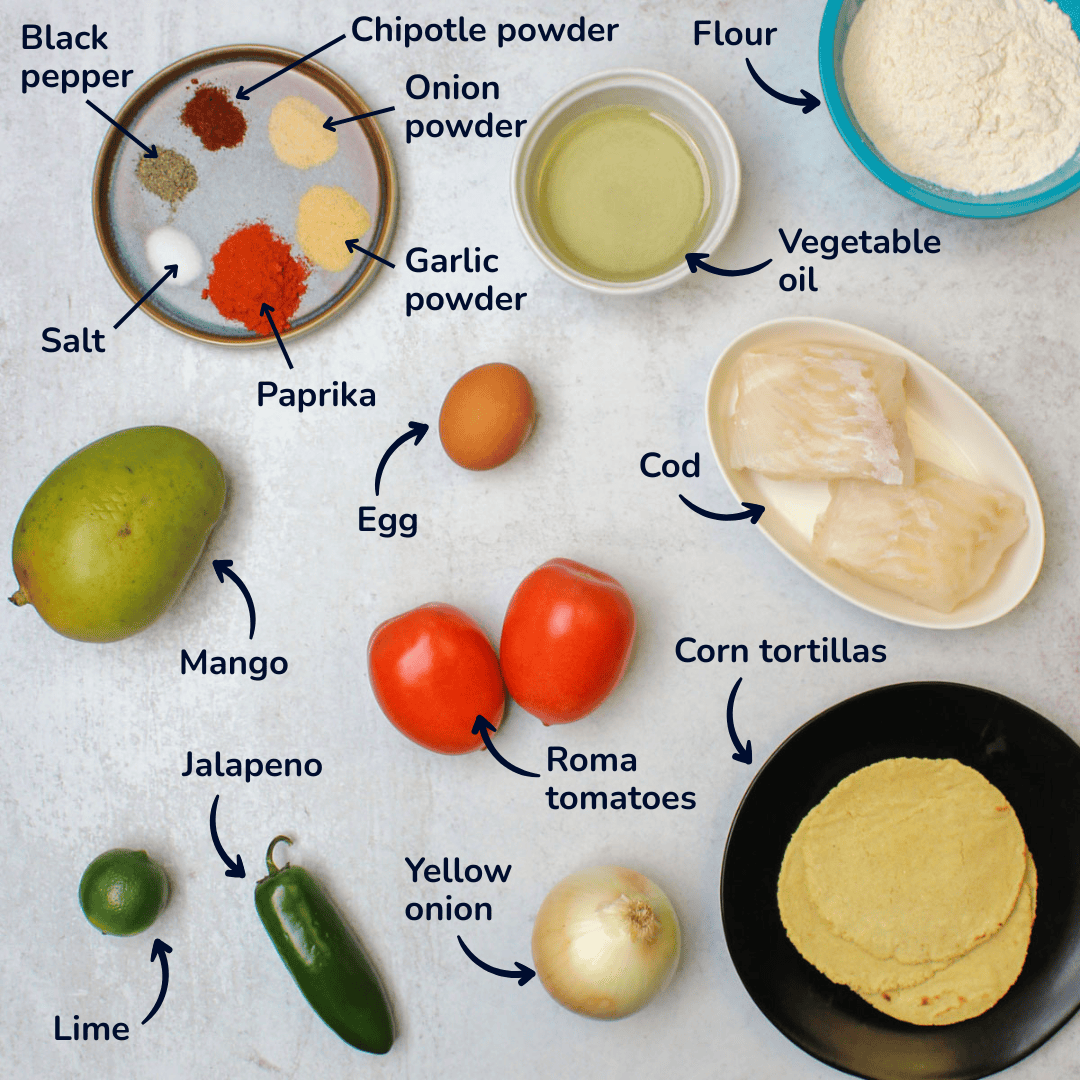An ingredient layout for fried fish tacos with mango salsa including: cod, corn tortillas, onion, tomato, mango, jalapeno, lime, flour, oil, egg, and spices.