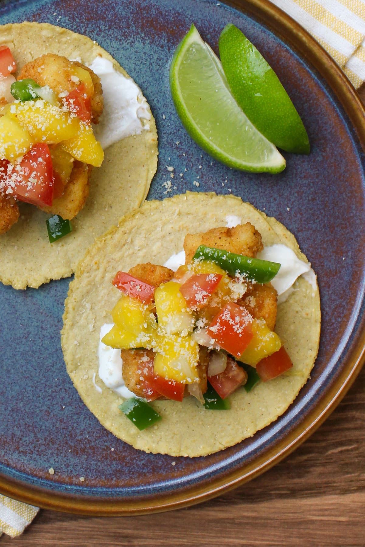 A fried cod taco on a corn tortilla with lime crema, mango salsa, and cotija cheese.