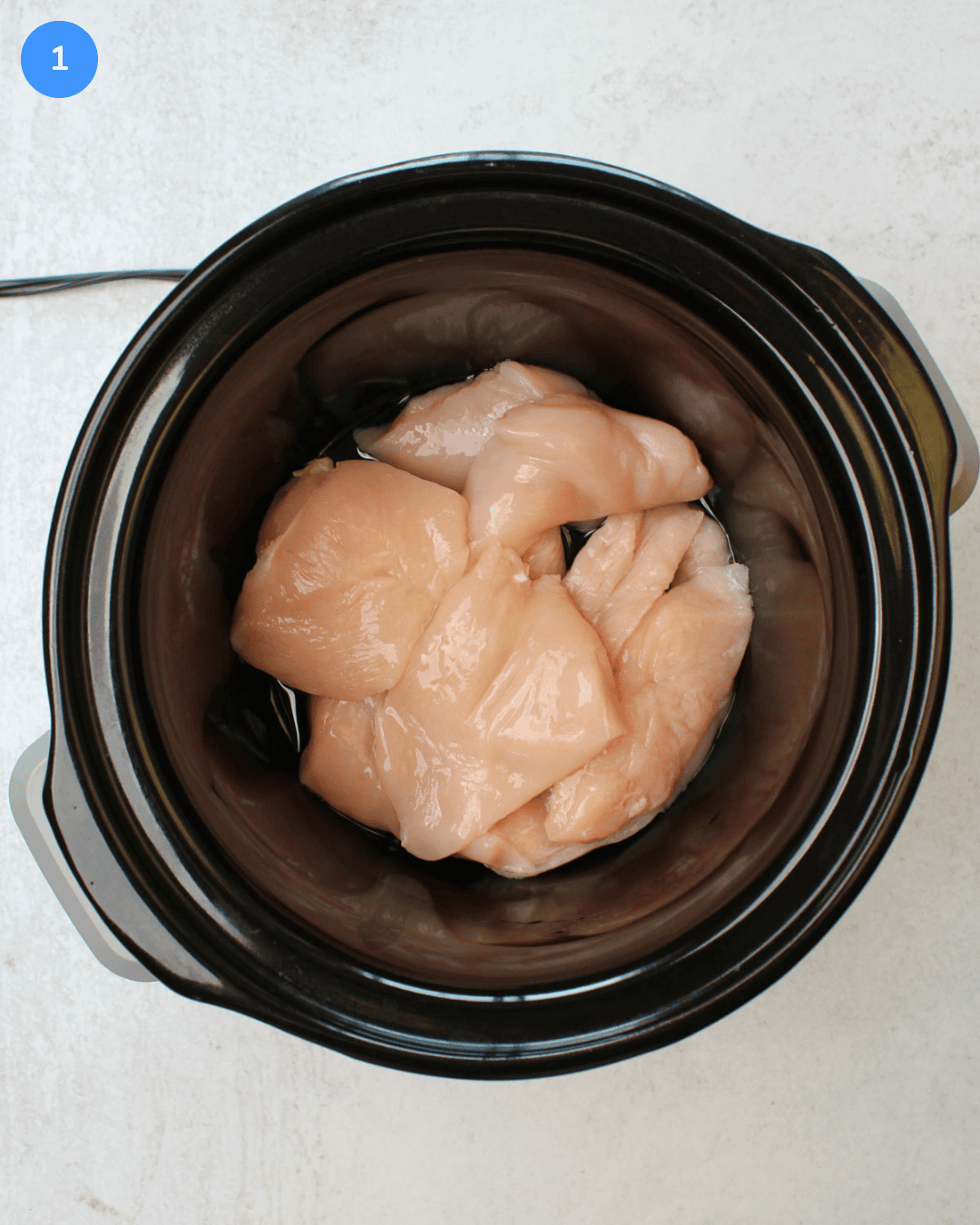 A crockpot with raw chicken breast sitting in it.