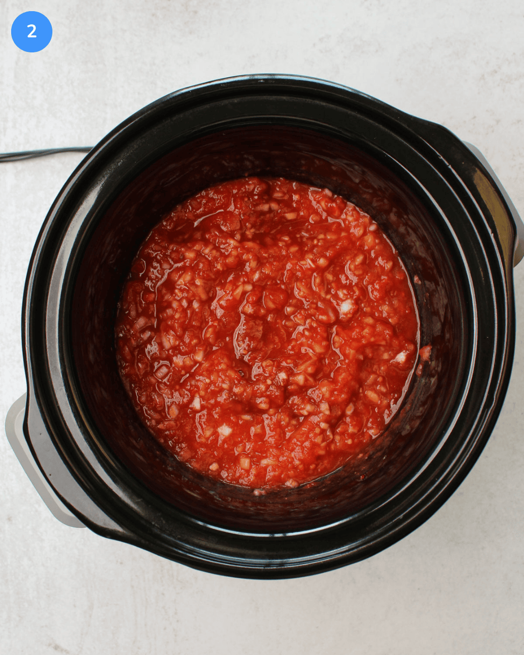A crockpot with crushed tomatoes, onion, garlic, brown sugar, soy sauce, ginger, gochujang, and chicken in it.