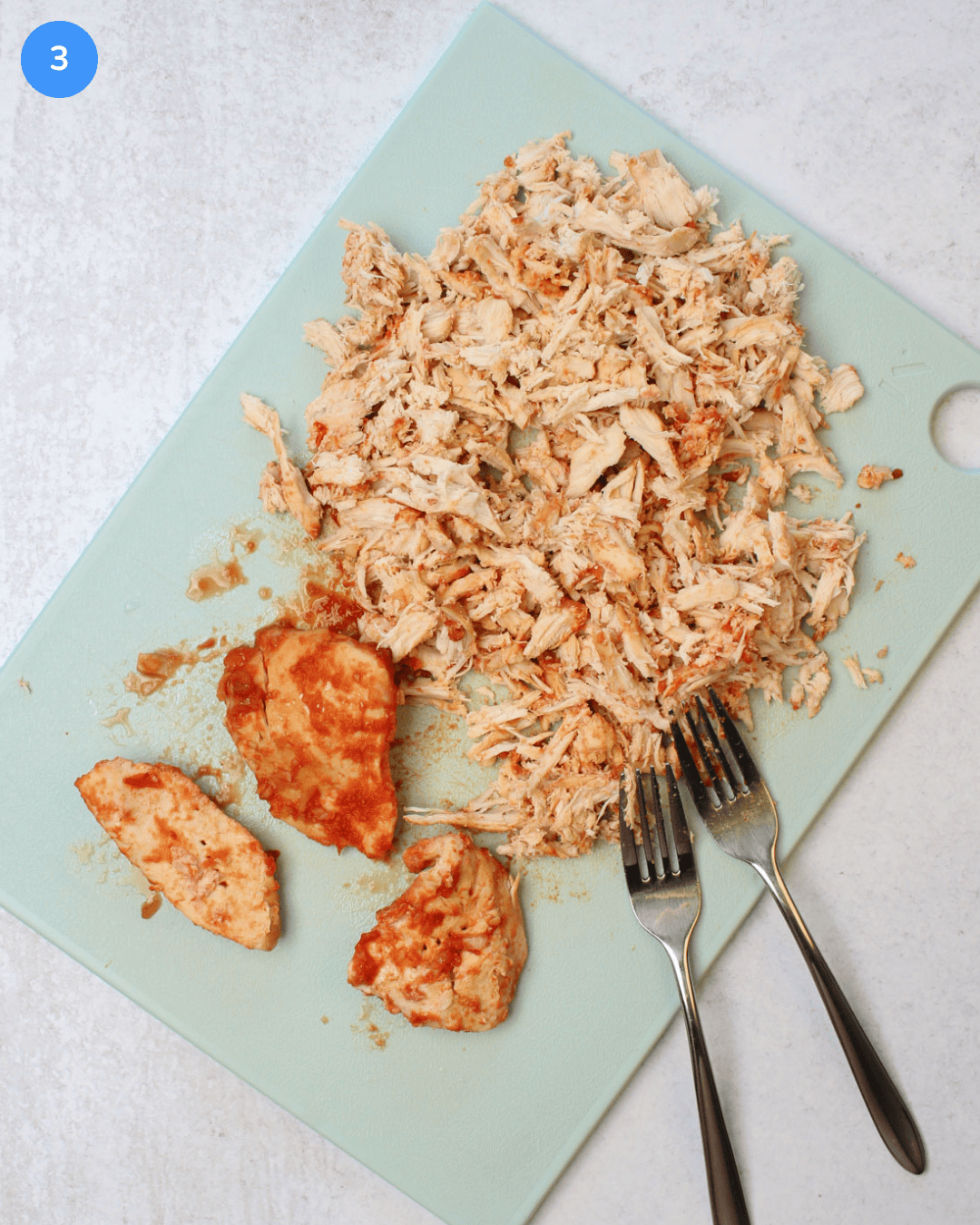 Freshly cooked gochujang chicken being shredded on a blue cutting board.