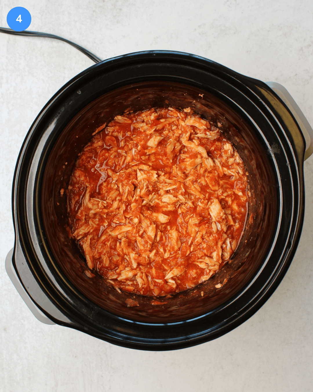 A black slow cooker with freshly cooked shredded gochujang chicken in it.