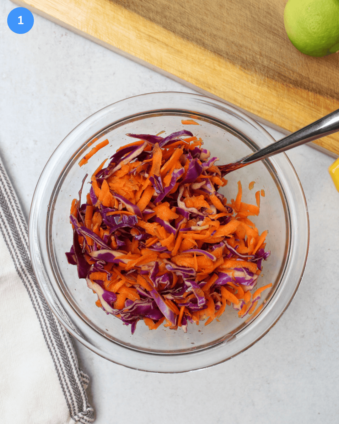 A small glass bowl of shredded carrots and red cabbage tossed with lime juice and salt.