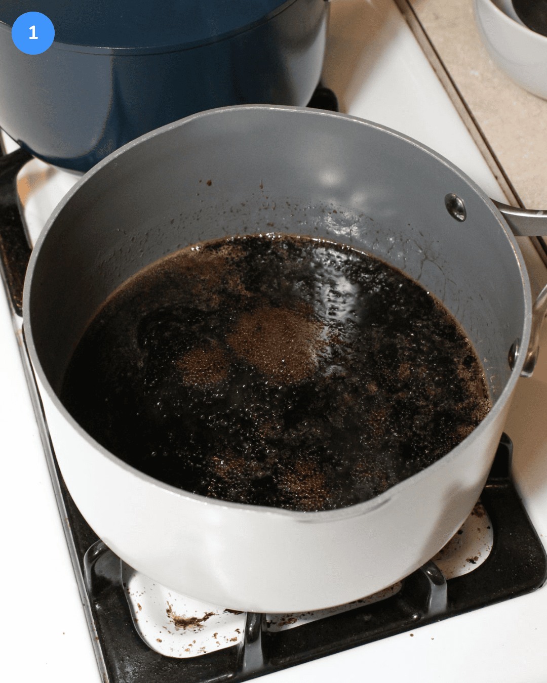 Step 1 of crispy chicken rice bowls. A ceramic saucepan with a sesame soy glaze simmering in it on the stove.