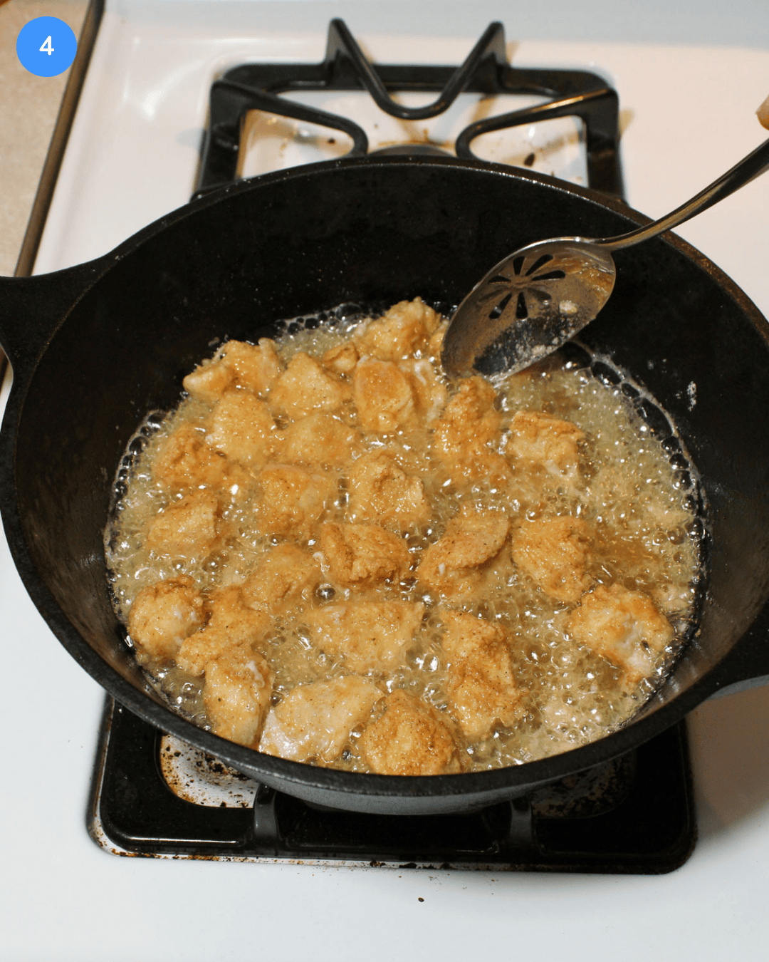 Step 4 of crispy chicken rice bowls. A deep walled cast iron pan with crispy coated chicken frying in oil on the stove.