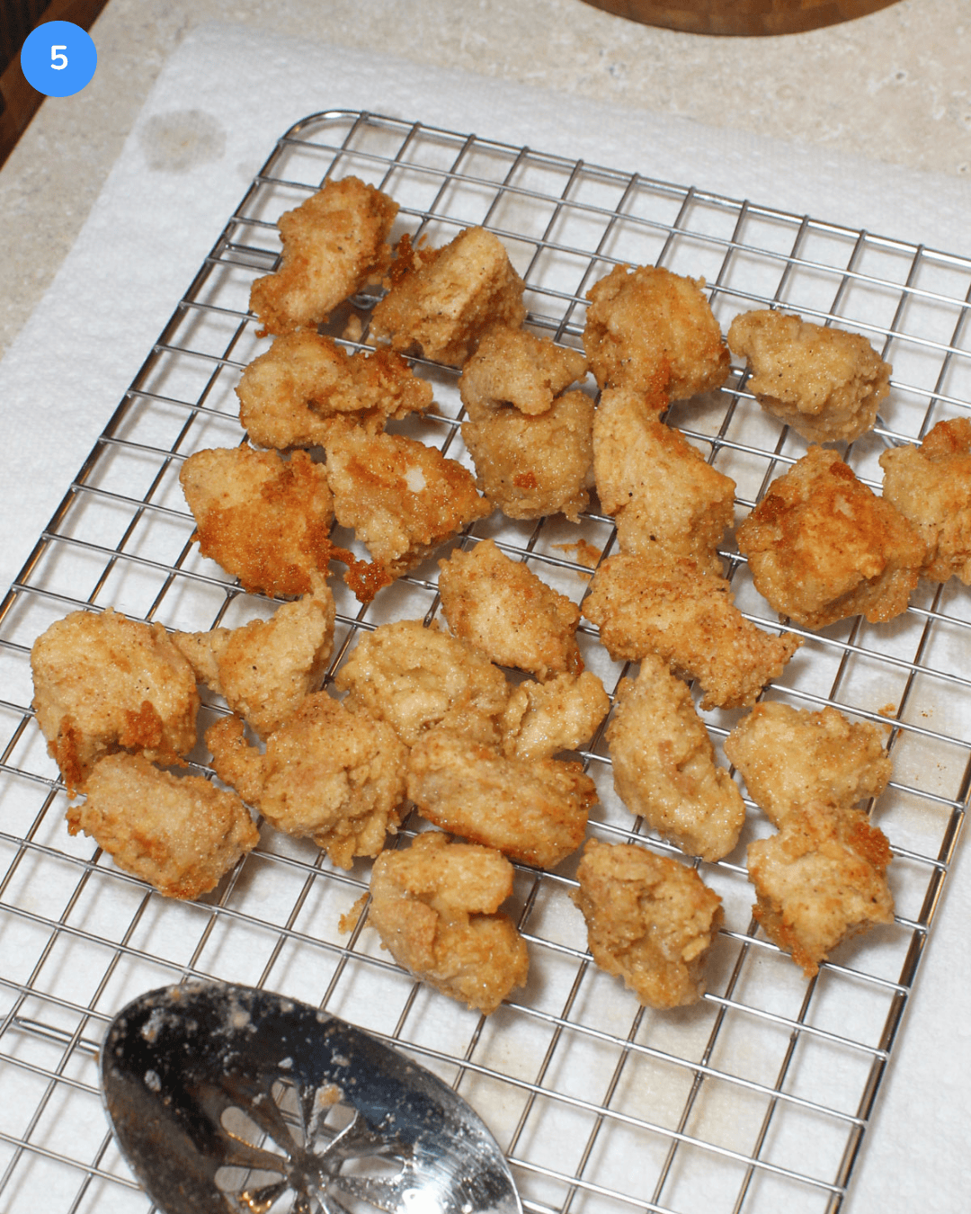 Step 5 of crispy chicken rice bowls. Bite size pieces of crispy fried chicken draining on a wire rack positioned above paper towels.