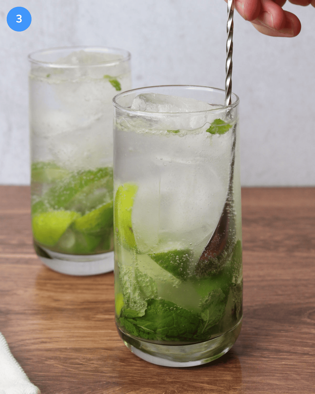 A mojito mocktail being stirred with a bar spoon in a tall Collins glass.