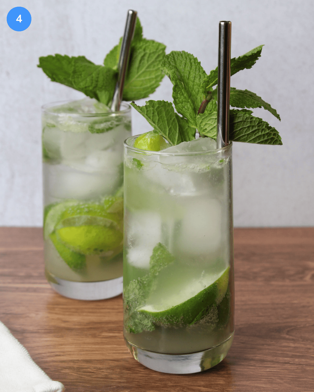 Two freshly made mojito mocktails in Collins glasses, garnished with a fresh mint sprig and served with a stainless steel straw.