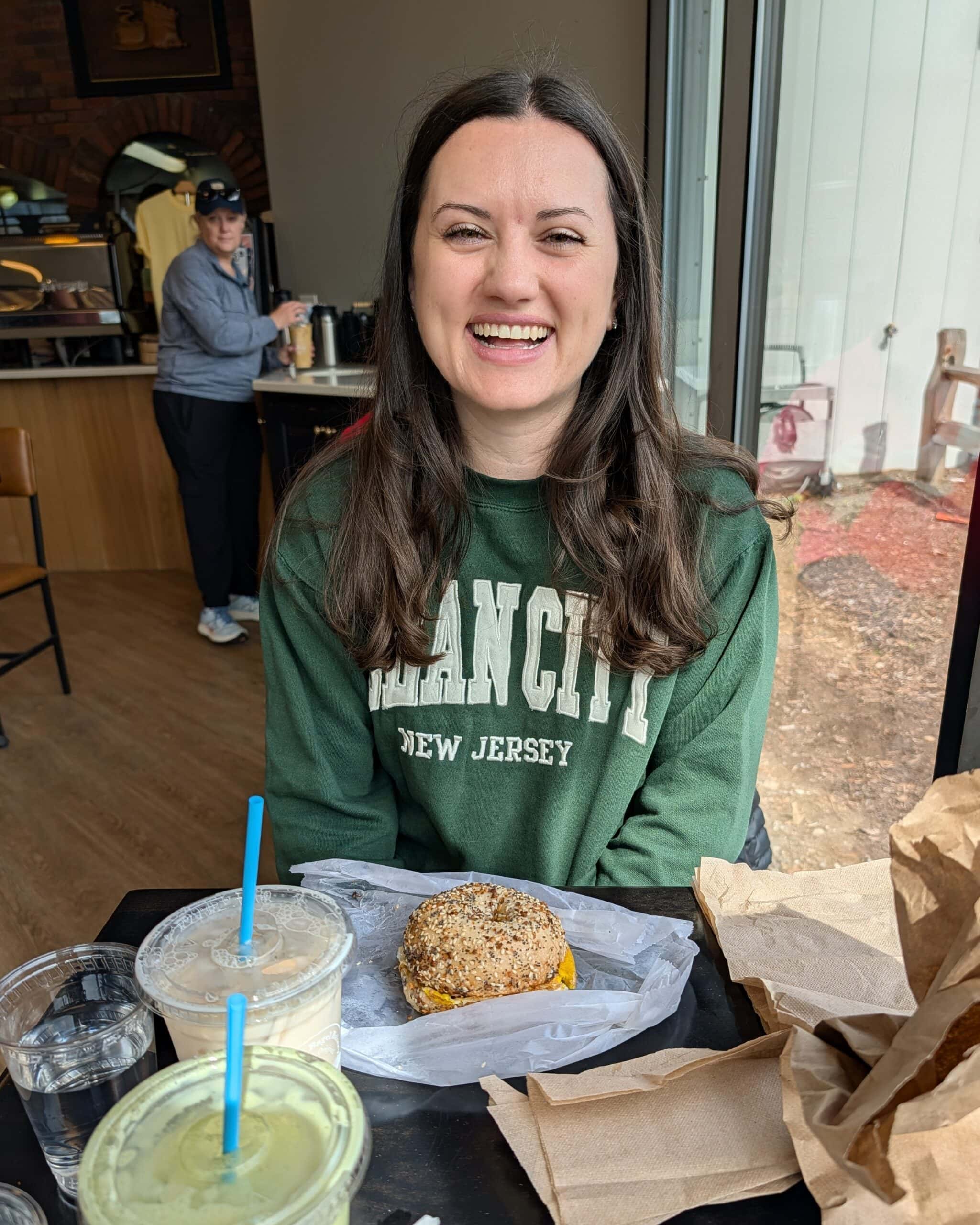 Nicole at a bagel shop with a breakfast sandwich and iced chai latte.