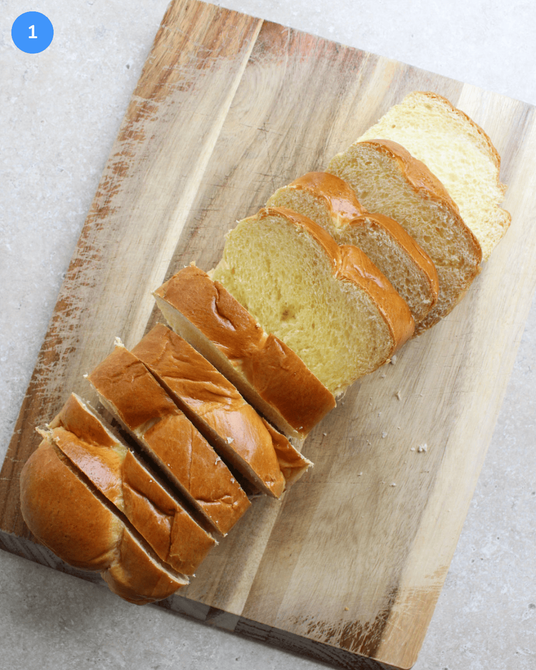 A wood cutting board with a freshly sliced loaf of brioche bread on it.