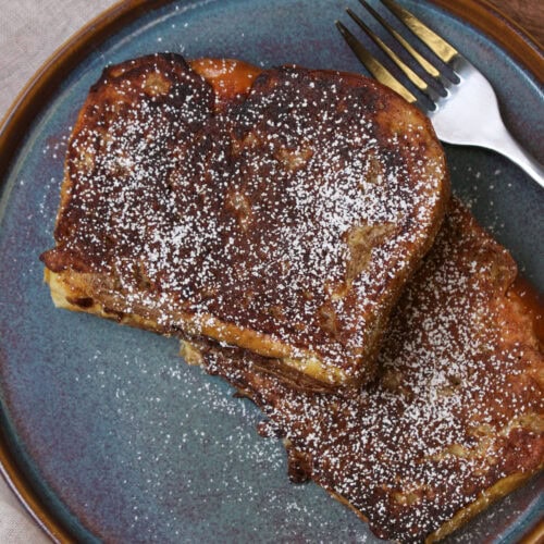 A blue stone plate with powdered sugar dusted brioche French toast stuffed with nutella on it.