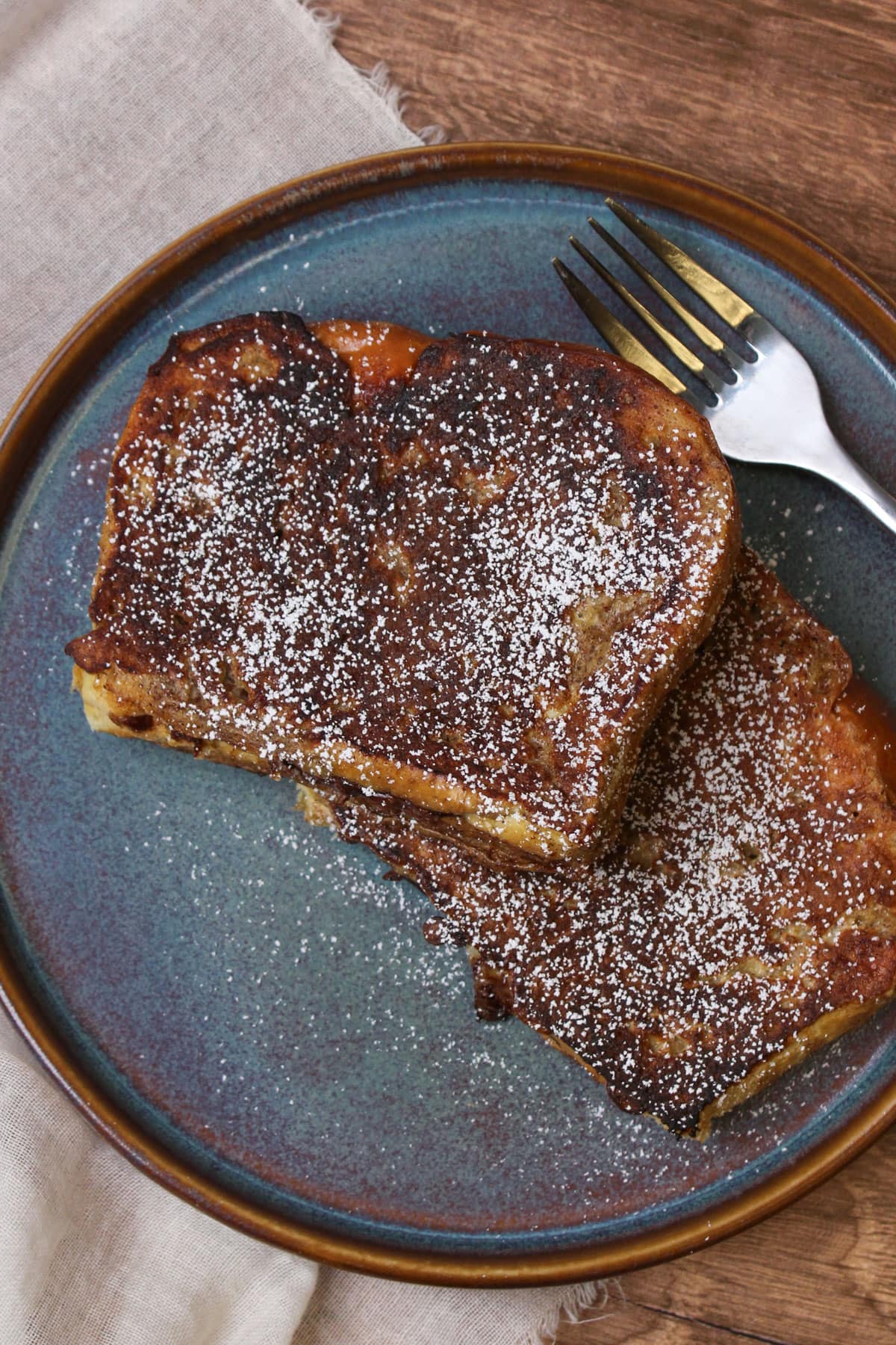 A blue stone plate with powdered sugar dusted brioche French toast stuffed with nutella on it.