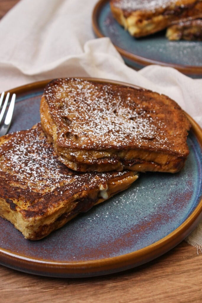 Two slices of Nutella stuffed brioche french toast dusted with powdered sugar and served on a blue stoneware plate.