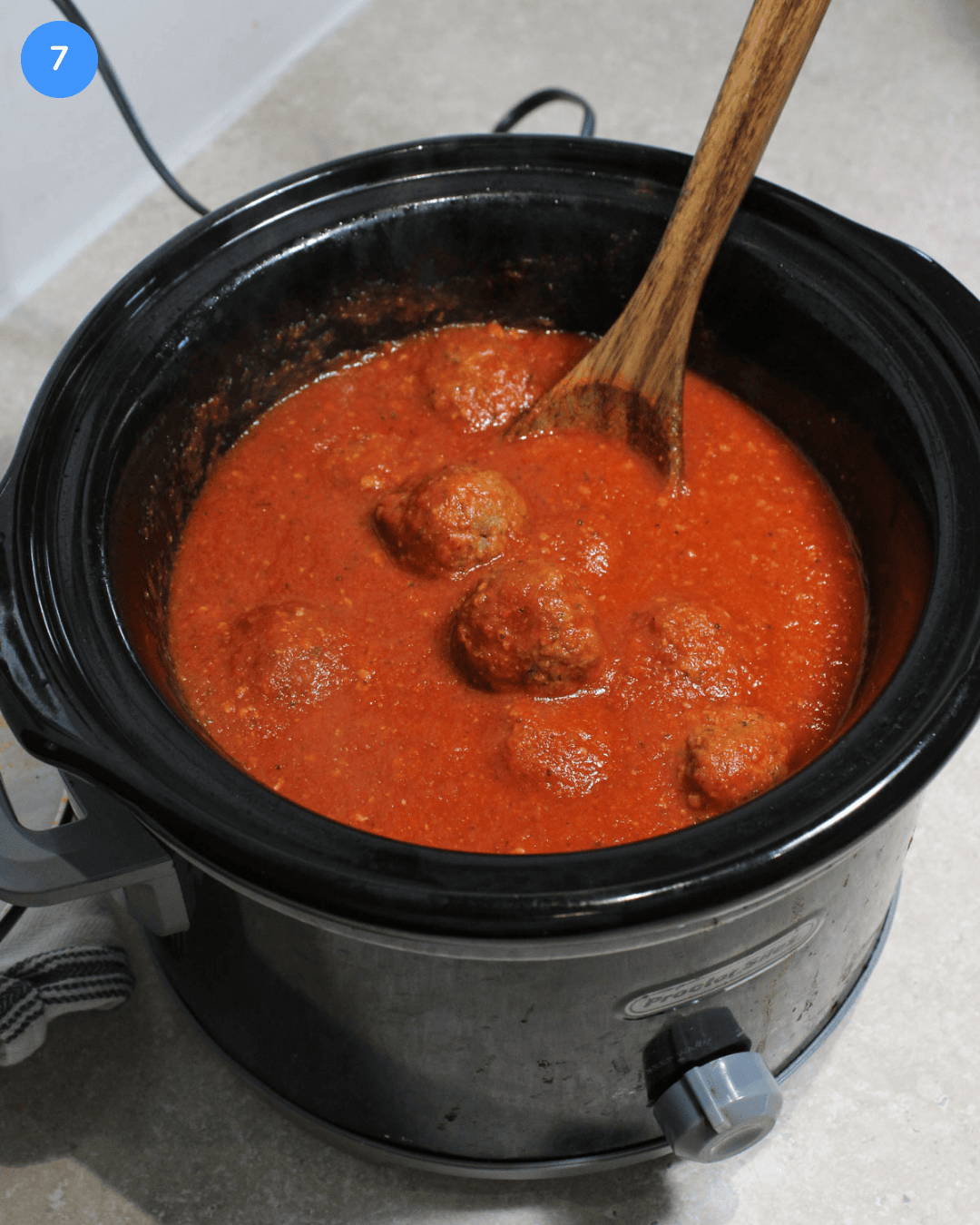 Step 7: A bright red pasta sauce and cooked meatballs in a slow cooker.