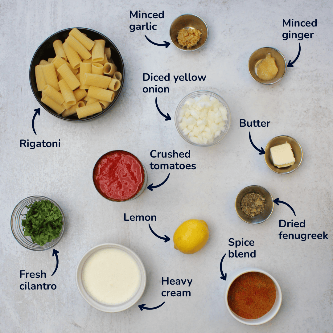 Ingredients with labels for making tikka masala pasta: rigatoni, minced garlic, minced ginger, yellow onion, butter, crushed tomatoes, lemon, cilantro, heavy cream, and spices.
