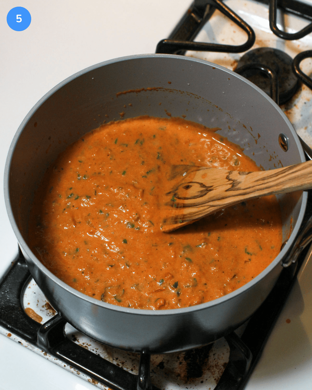 Step 5: A sauce pot of a bright red tikka masala sauce being cooked with bits of green cilantro mixed in.