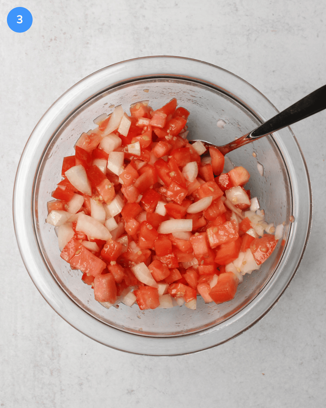 A glass mixing bowl of freshly made tomato bruschetta topping, made with diced tomato, diced onion, garlic, salt, and olive oil.