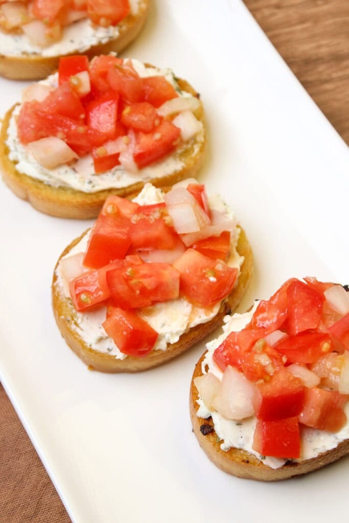 A white ceramic dish of freshly made tomato bruschetta crostini topped with spreadable cheese.