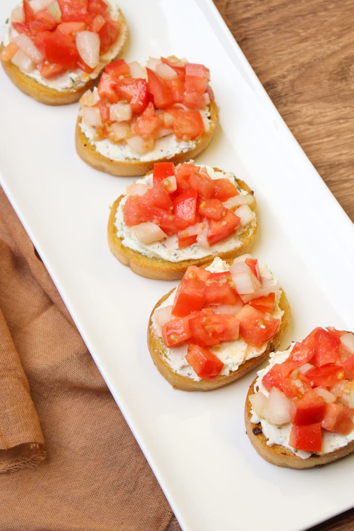 A long white serving platter of tomato bruschetta crostini with alouette garlic and herb cheese spread.