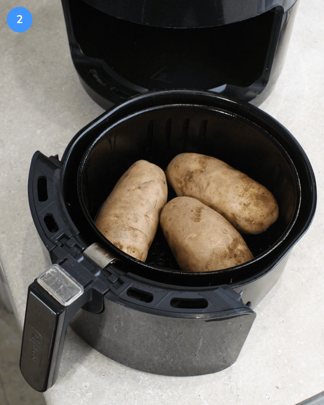 Step 2: Three russet potatoes in an air fryer basket.