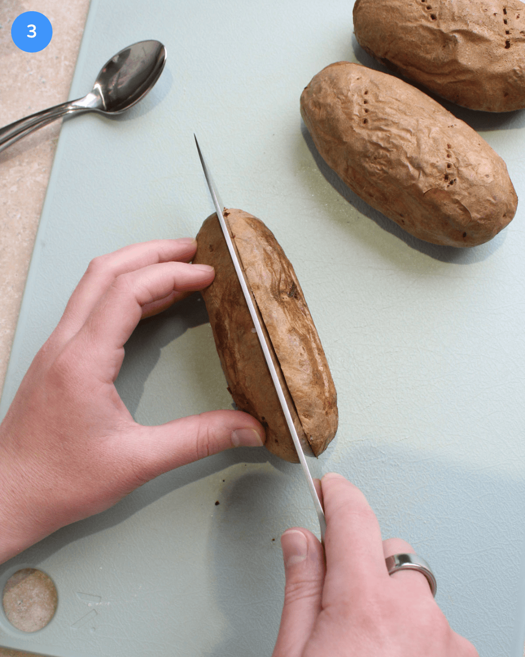 Step 3: An air fried russet potato being sliced in half on a cutting board.