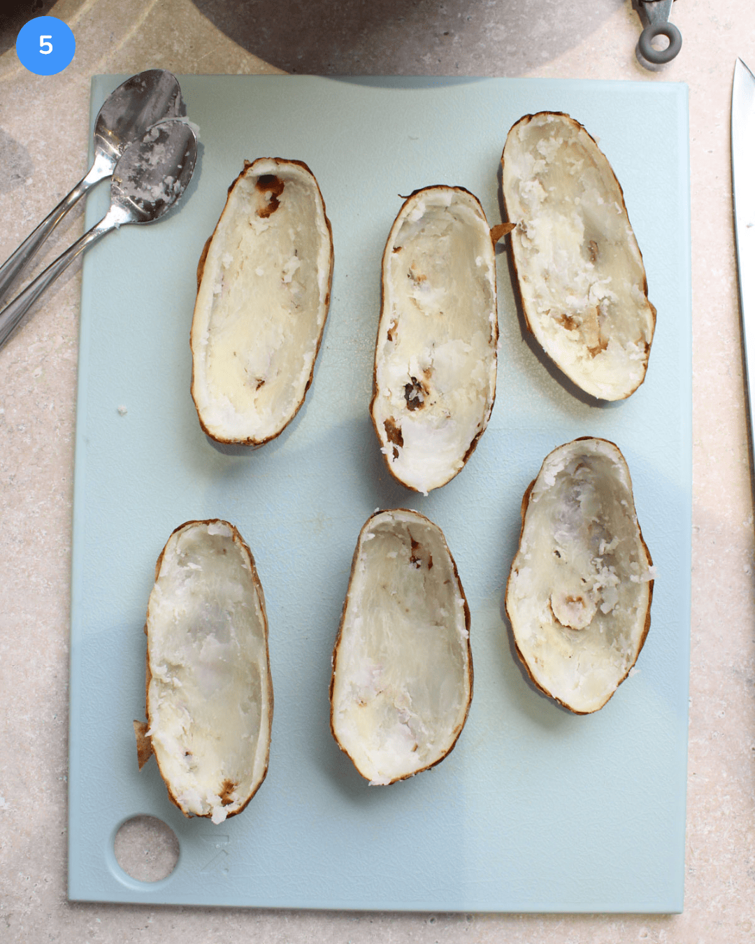Step 5: 6 halves of air fried potato skins, that have the insides scooped out, sitting on a cutting board.