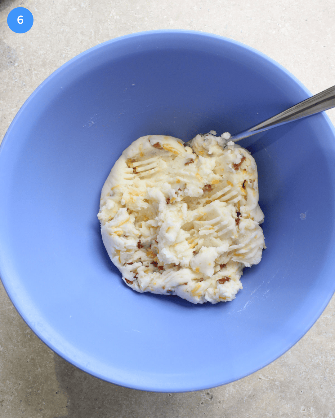 Step 6: A mixed filling made with potato cheese, bacon bits, butter, and heavy cream in a blue mixing bowl.
