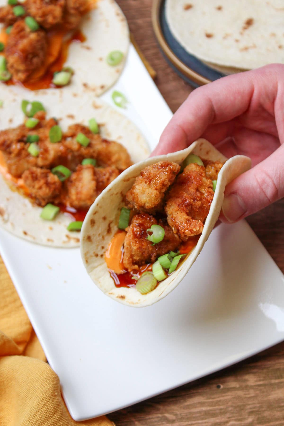 A folded fried chicken taco in a flour tortilla with sriracha aioli, asian sesame glaze, and scallions.