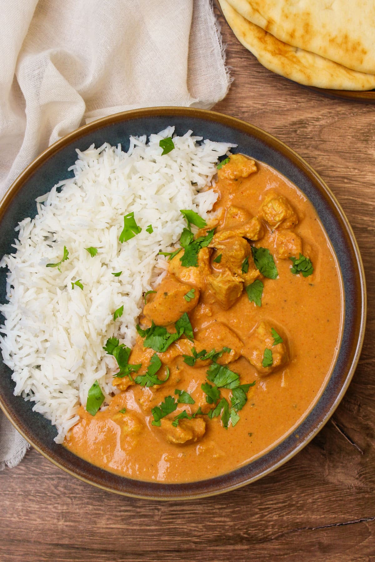 A blue stone bowl of chicken tikka masala and rice garnished with fresh cilantro.