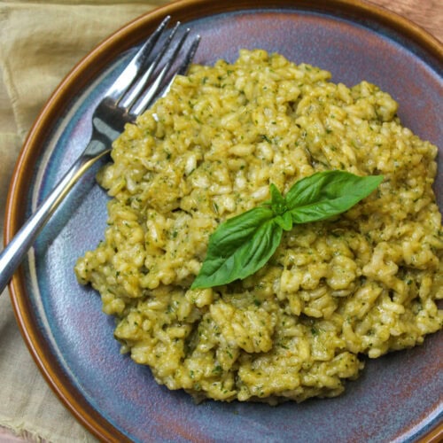Creamy pesto risotto garnished with fresh basil on a blue stoneware plate.
