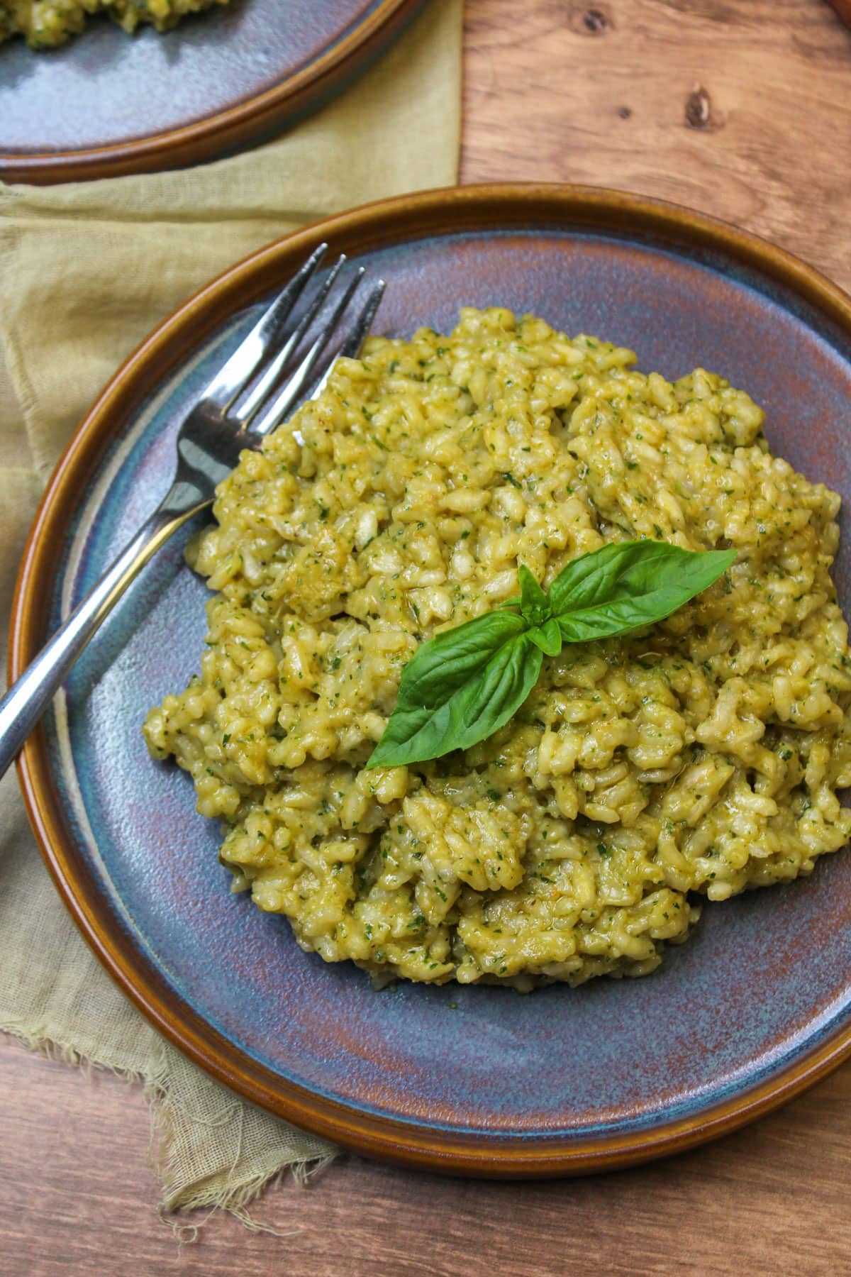 Creamy pesto risotto garnished with fresh basil on a blue stoneware plate.