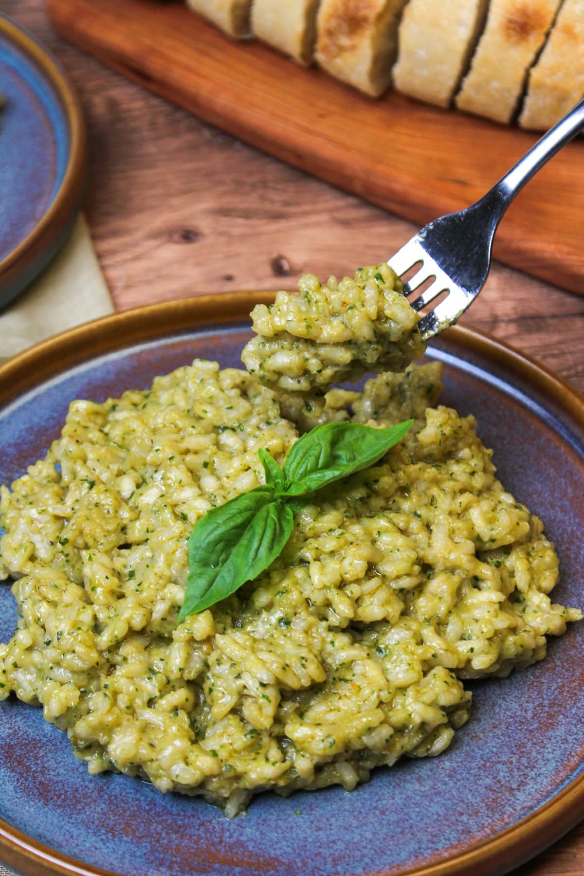 Homemade pesto risotto on a blue stoneware plate garnished with fresh basil being scooped up with a fork.